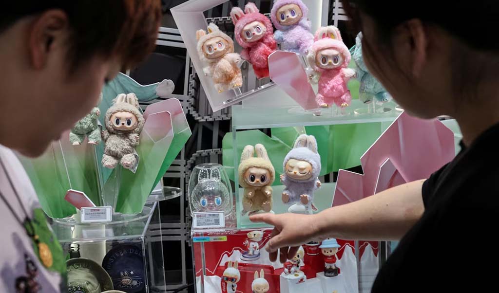 Two shoppers examining a colorful display of Labubu collectible plush and vinyl figures in various pastel colors at a Pop Mart store.