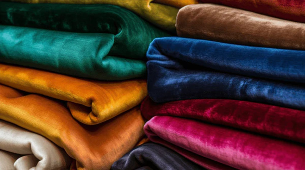 Piles of soft velvet fabric in rich colors including green, gold, blue, and red, ideal for making luxury plush toys.