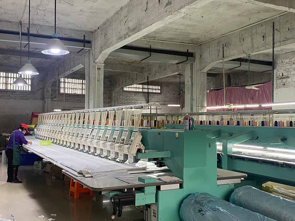 Worker operating a multi-head embroidery machine in a plush toy factory, stitching detailed designs on fabric for mass production.