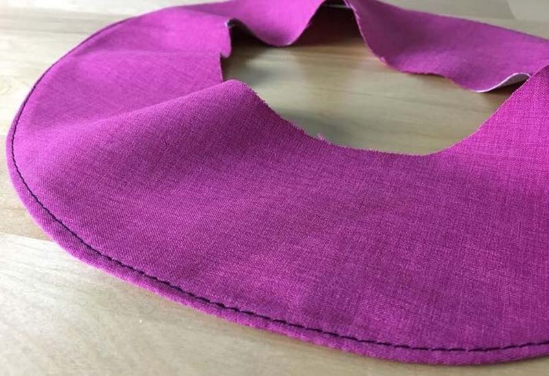 Close-up of a curved magenta fabric piece with a clean stitched edge, showing a finished facing or hem technique used in sewing and plush toy construction.