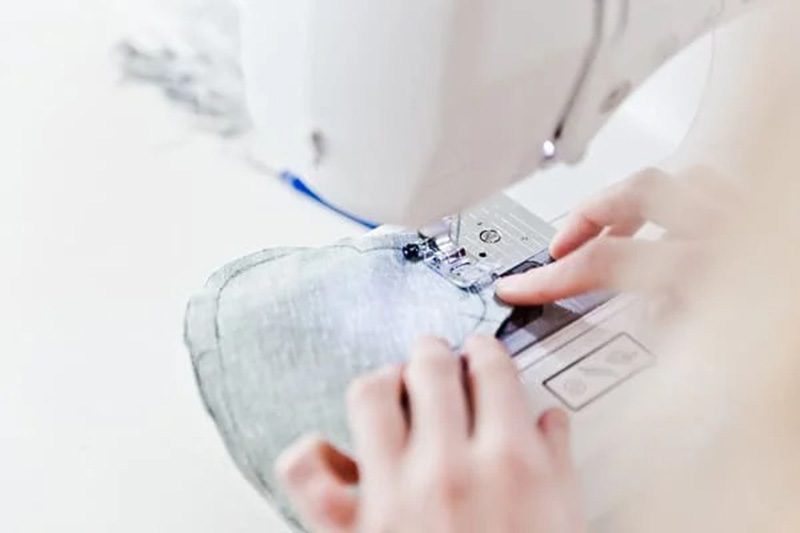 Hands guiding soft plush fabric through a sewing machine, stitching the curved seam for a stuffed toy.