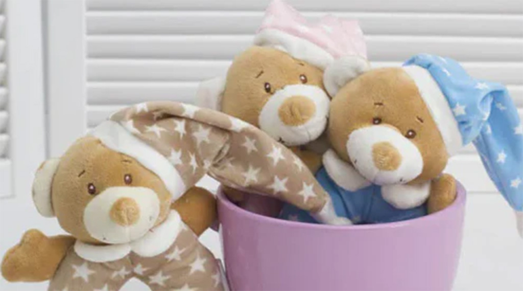 Three soft teddy bears wearing star-patterned pajamas and nightcaps sitting together in a purple container.