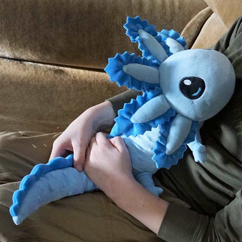 Child holding a blue axolotl plush toy on their lap.