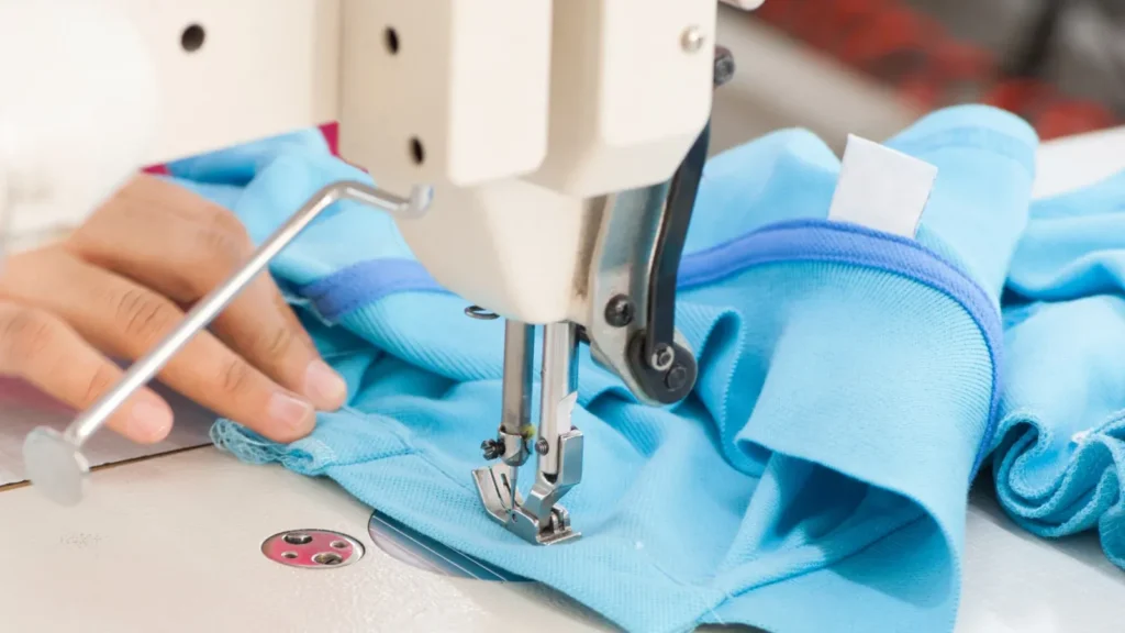 Close-up of hands guiding blue fabric through an industrial sewing machine during precise stitching.