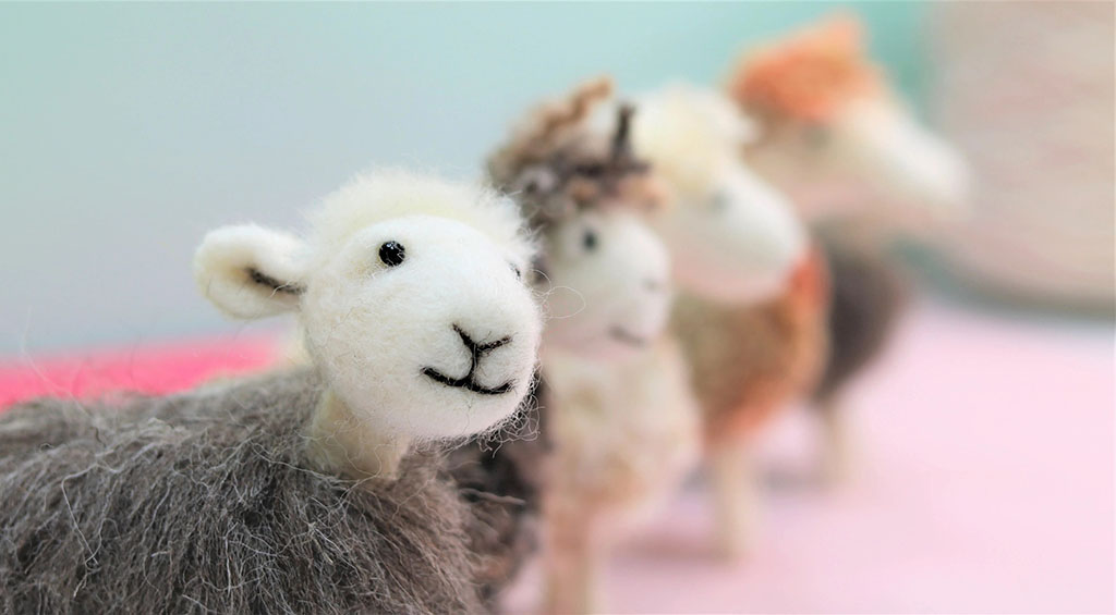 A close-up of handmade felted sheep plush figures, with one sheep in focus and others blurred in the background.