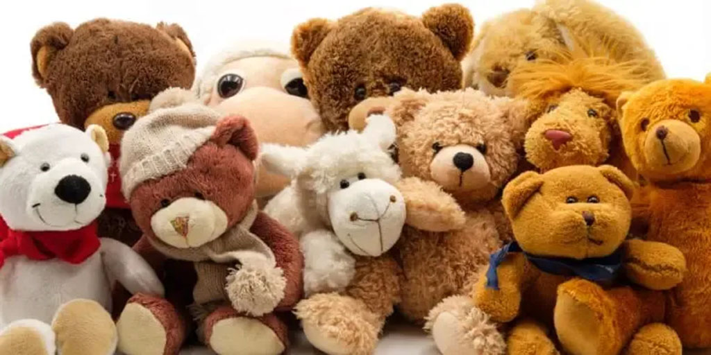 A collection of assorted plush toys including teddy bears, a polar bear, a lion, and a sheep, arranged closely together in warm, soft colors.
