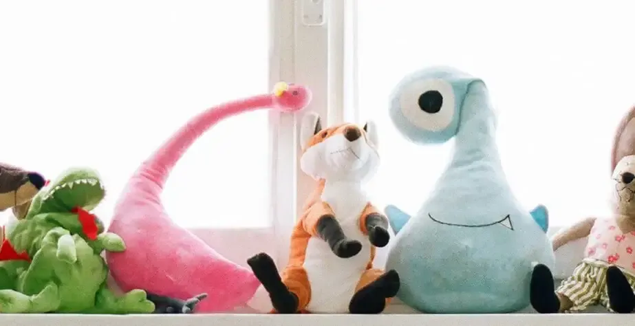 Colorful plush toys—including a pink dinosaur, orange fox, and blue monster—displayed on a white windowsill.