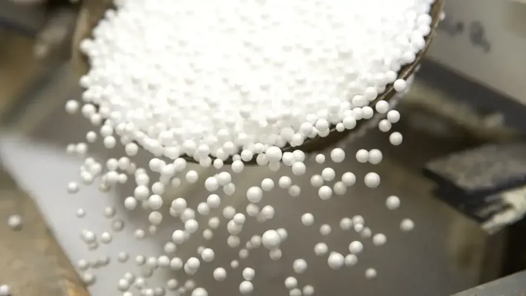 Close-up of white polystyrene microbeads pouring from a container, showing the small round pellets commonly used as stuffing for bean bags and soft toys.
