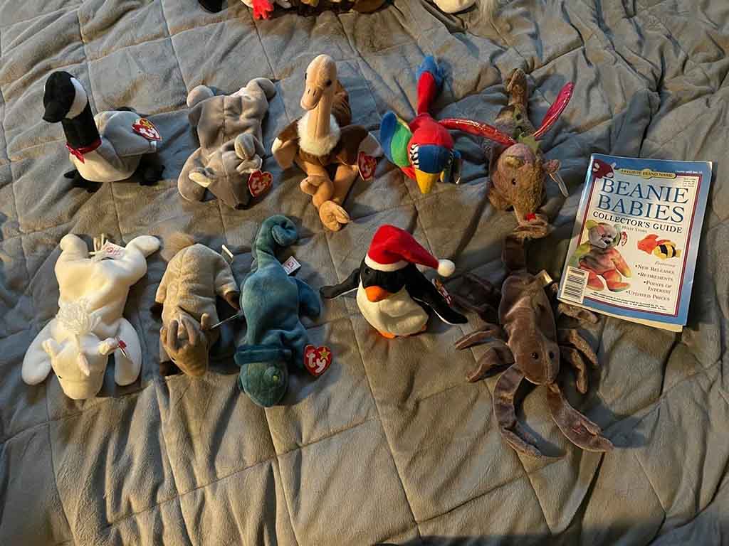Assorted Beanie Babies arranged on a bed with a collector’s guide book.