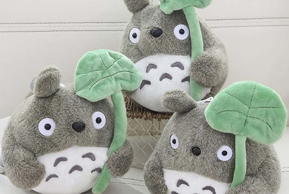 Three gray Totoro plush toys holding soft green leaf props, displayed on a light-colored surface.