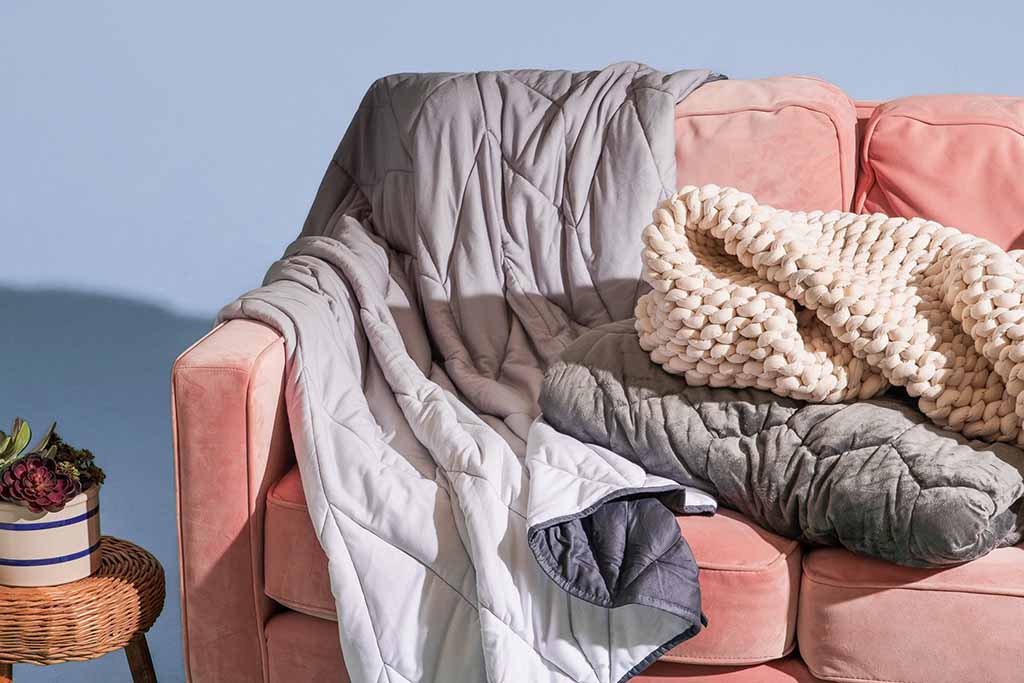 “Weighted blankets and chunky knit throw draped over a pink sofa.”