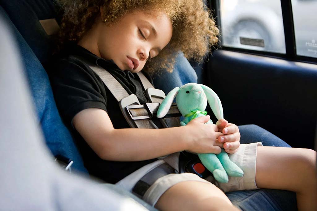 Young child sleeping in a car seat while holding a small green plush bunny toy, highlighting comfort, safety, and emotional bonding with stuffed animals.