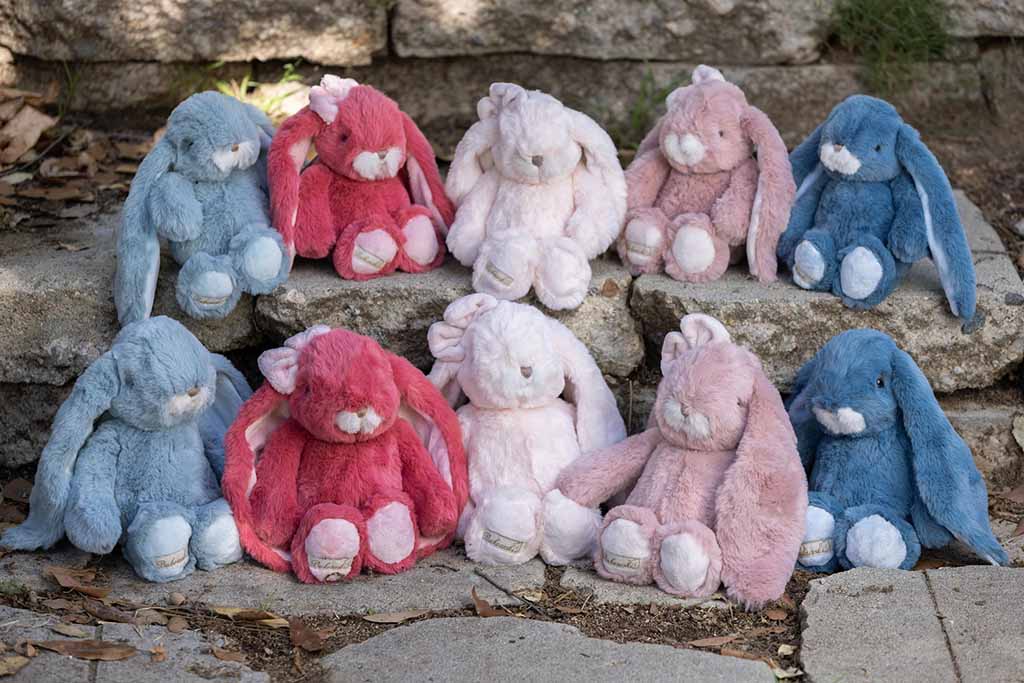 Group of pastel-colored plush bunnies with long floppy ears sitting on stone steps outdoors.