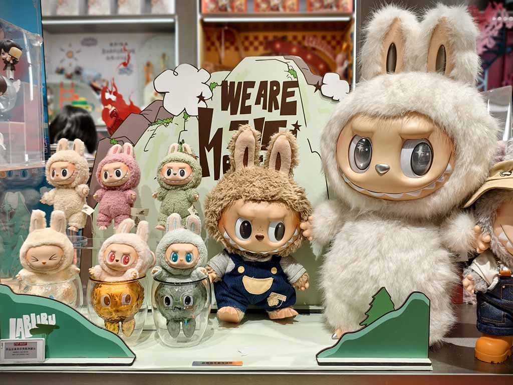 Collection of Labubu plush toys and vinyl figures in different colors and sizes displayed on a themed shelf with a “We Are Monsters” background.