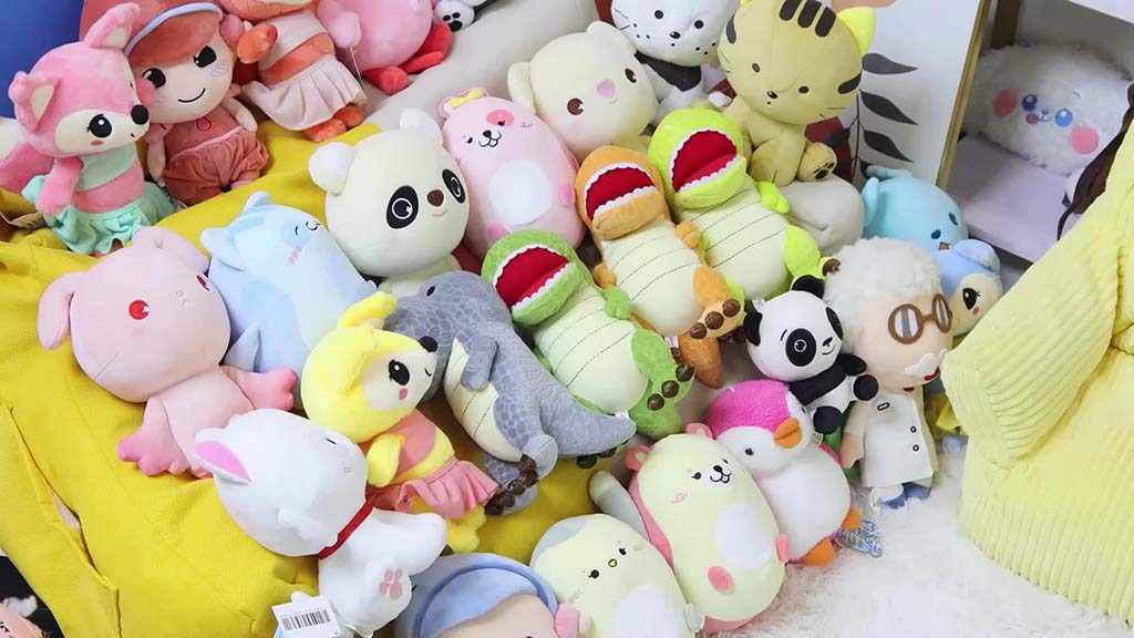 A colorful assortment of plush toys including animals, characters, and fantasy creatures arranged closely together on soft cushions.