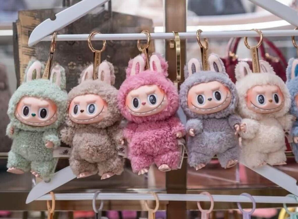 Row of colorful Labubu plush keychains in pastel costumes hanging on a white rack, each with bunny ears and expressive cartoon faces.