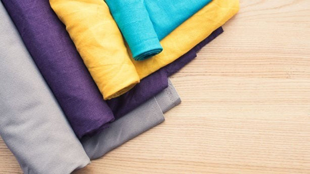 Assorted linen fabric rolls in teal, yellow, purple, and gray displayed on a wooden surface, showing natural texture and color options for textile and toy production.