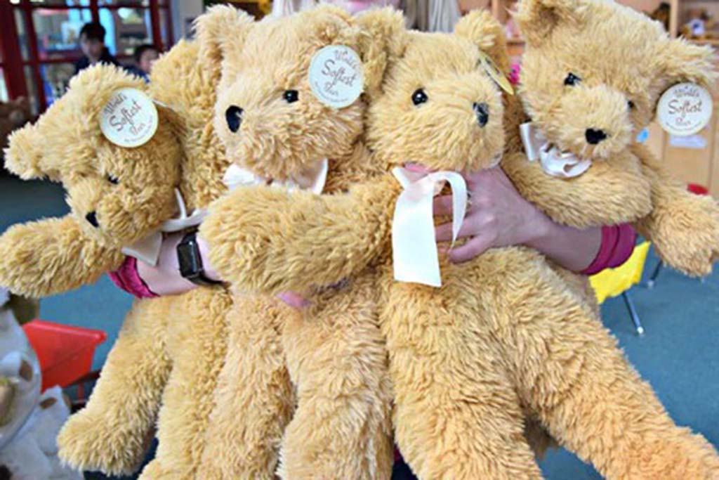 A person holding several large golden teddy bears with white ribbons and tags inside a toy store.