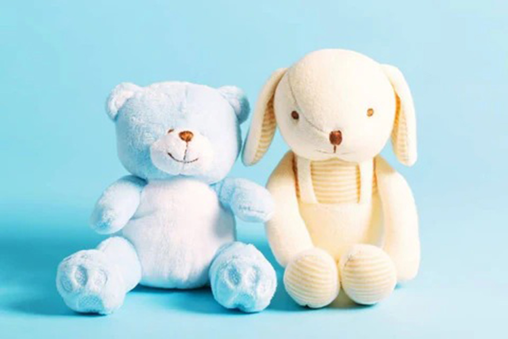 Light blue teddy bear and cream bunny plush toy sitting on a pastel blue background, showcasing soft textures and baby-safe stuffed animal design.