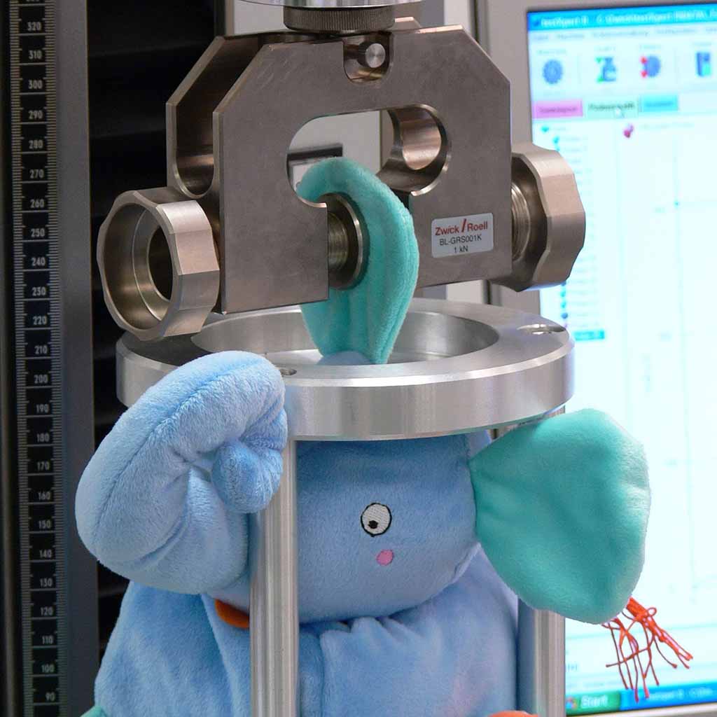 Blue plush toy undergoing tensile strength test with laboratory equipment to ensure safety and compliance with EN71 toy standards.