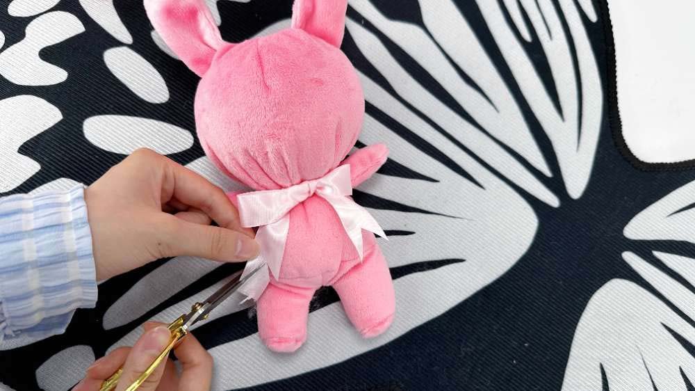 Hands trimming a tag from a pink plush bunny with scissors.