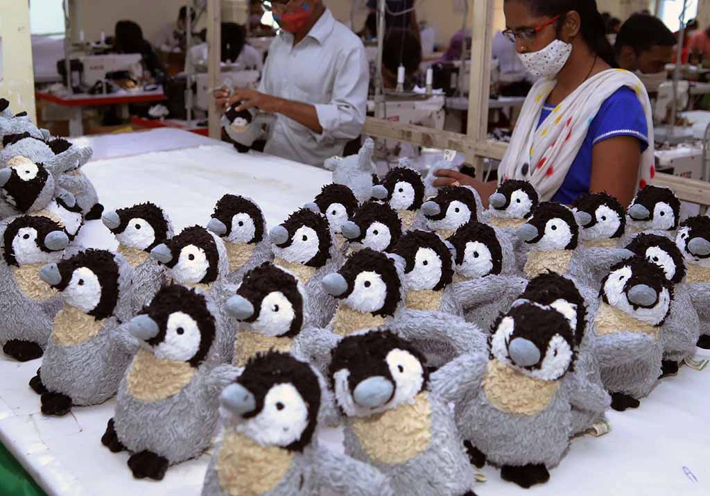 Factory workers inspecting and assembling rows of identical gray and white penguin plush toys on a production table.