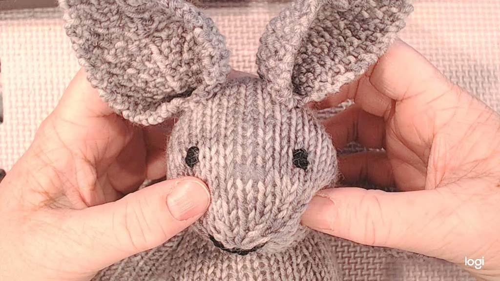 Close-up of hands holding and adjusting a handmade knitted bunny toy, showing detailed yarn texture, stitched facial features, and soft knitted ears, demonstrating craftsmanship and quality checking for handmade plush toys.