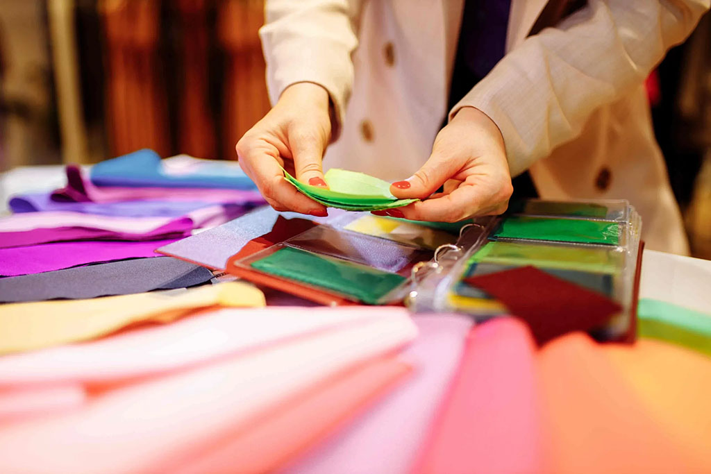 Person examining colorful fabric swatches spread across a table, comparing textile samples from a binder for material or color selection.