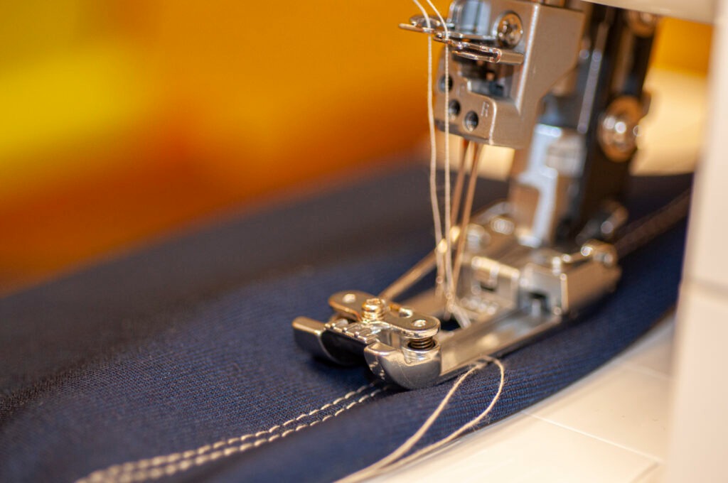 Close-up view of a sewing machine stitching a straight seam on dark blue fabric.