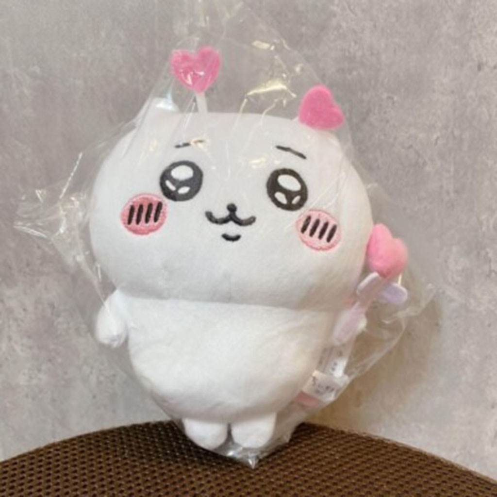 Small white plush toy with pink heart accents, rosy cheeks, and embroidered kawaii-style eyes, wrapped in clear plastic packaging.
