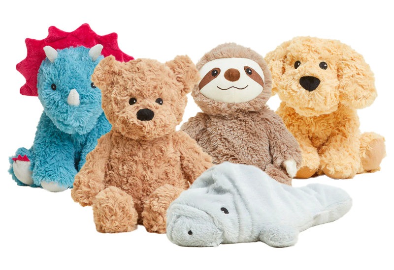 A group of soft, cuddly plush animals including a blue triceratops, brown teddy bear, sloth, golden puppy, and a light gray manatee, all arranged together against a white background.