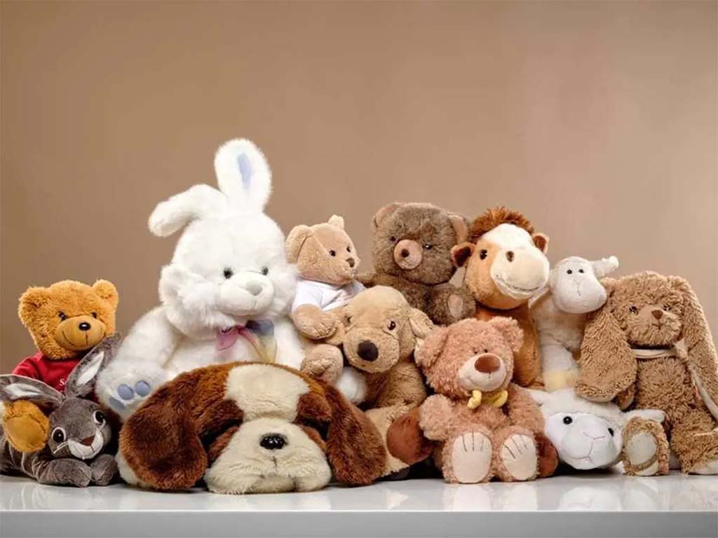 A large group of various plush animals, including bears, a bunny, a dog, a camel, a monkey, a rabbit, and a lamb, arranged closely together against a neutral background.