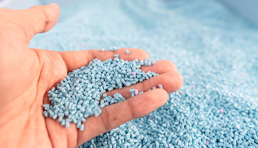 Hand holding small blue plastic pellets, commonly used as raw material for injection molding and toy production components.