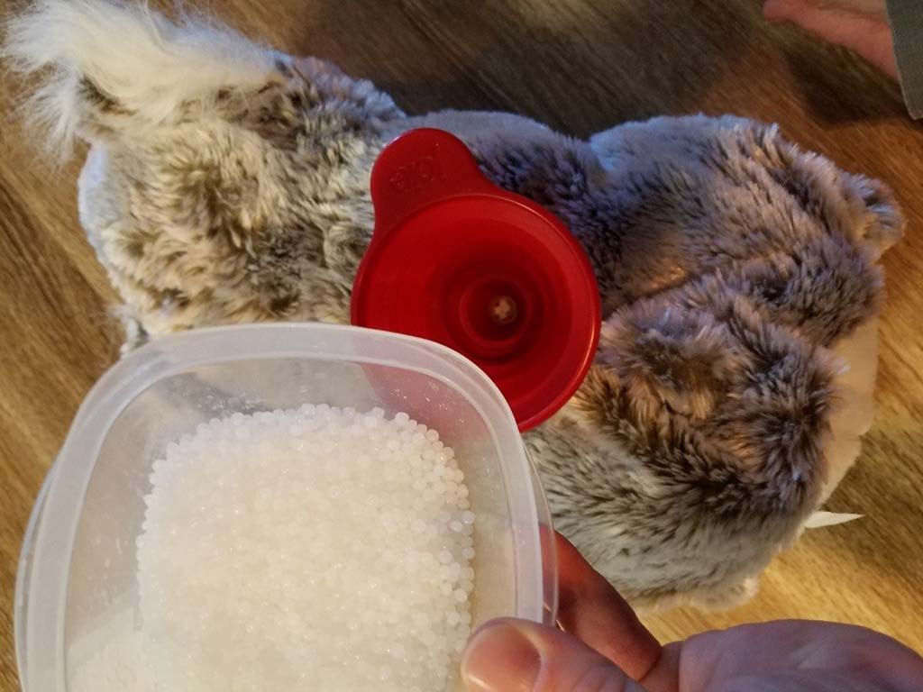 Close-up of poly-pellet beads being poured through a red funnel into a plush toy to add weight.