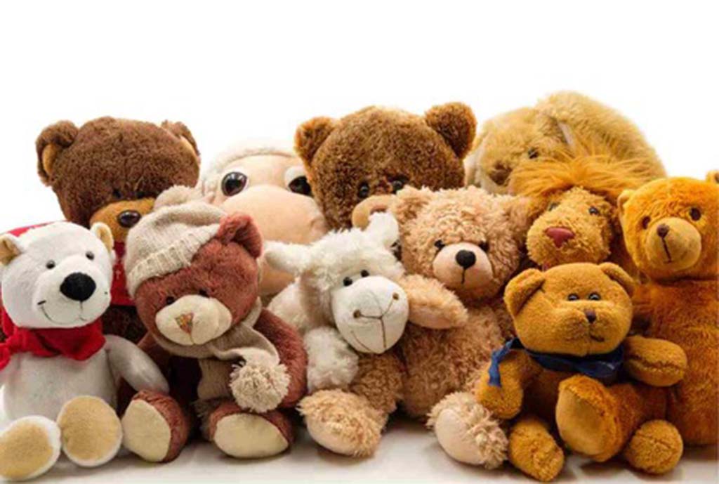 Collection of soft plush teddy bears in various shades of brown and cream, some wearing scarves and hats, sitting together against a white background.