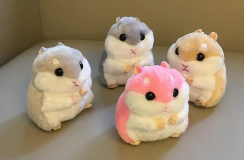Four round hamster plush toys in beige, gray, brown, and pink colors sitting together on a beige surface, featuring soft fur and adorable black eyes.