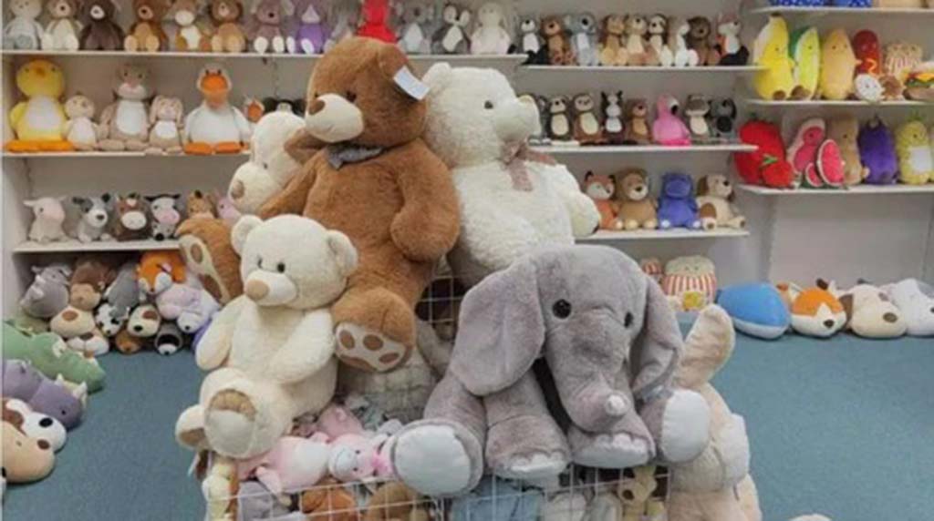 Large assortment of plush toys in a store, including teddy bears, elephants, and various animals arranged on shelves and in a central bin.