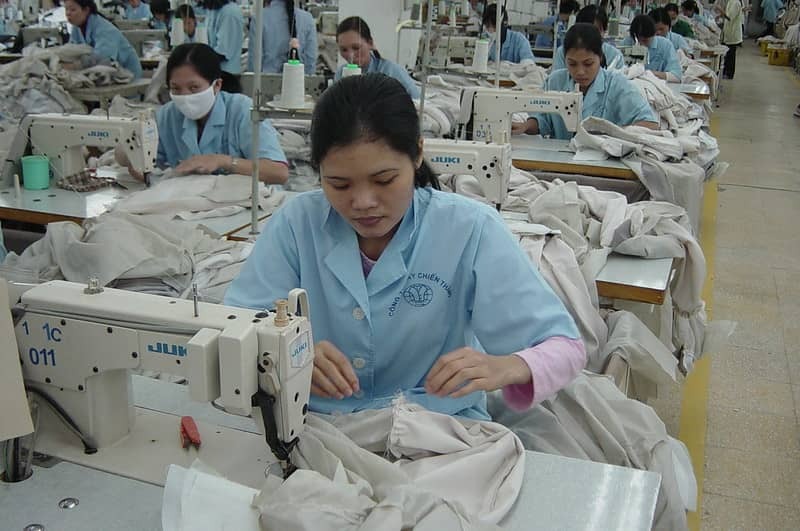 Workers in a garment factory using industrial sewing machines to stitch fabric pieces.