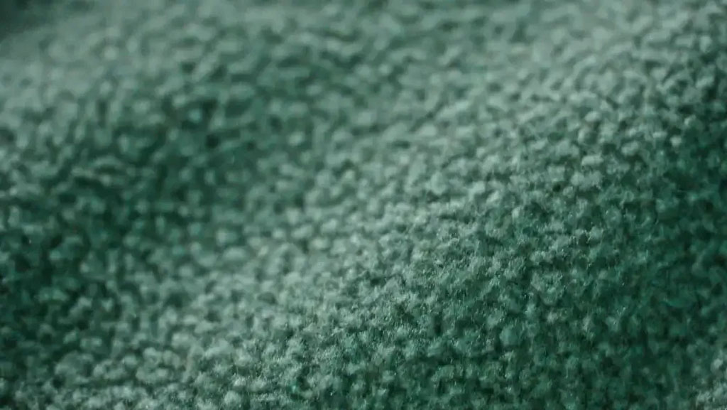 Close-up of green fleece fabric showing its soft, napped surface and warm, fuzzy texture commonly used for plush toys and winter garments.