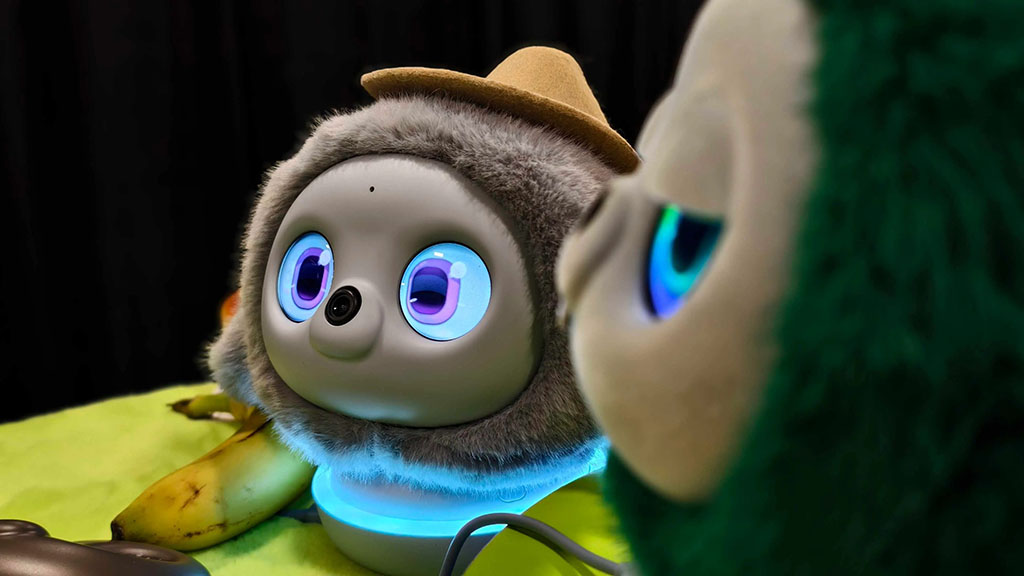 Close-up of two interactive robot plush characters with glowing blue eyes, one wearing a small hat, displayed on a table.
