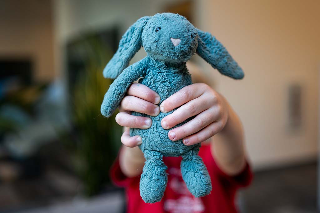 Child holding a worn blue stuffed bunny toy with both hands in a cozy indoor setting.