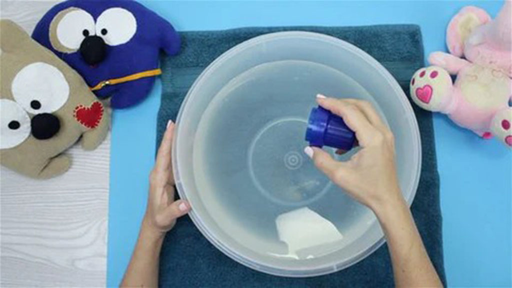 Hands preparing a basin of water with detergent for washing plush toys, with several stuffed animals placed around the setup.