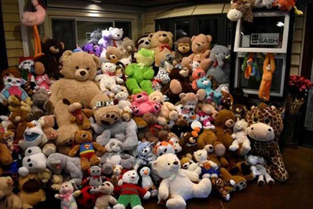 A large pile of assorted stuffed animals of many sizes and colors arranged in front of a house window