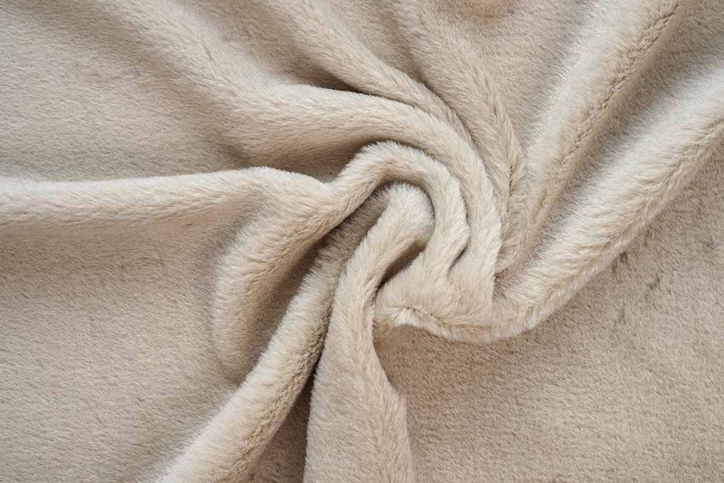 Beige short-pile plush fabric with smooth velvety texture, shown twisted to highlight its softness and dense fiber surface.