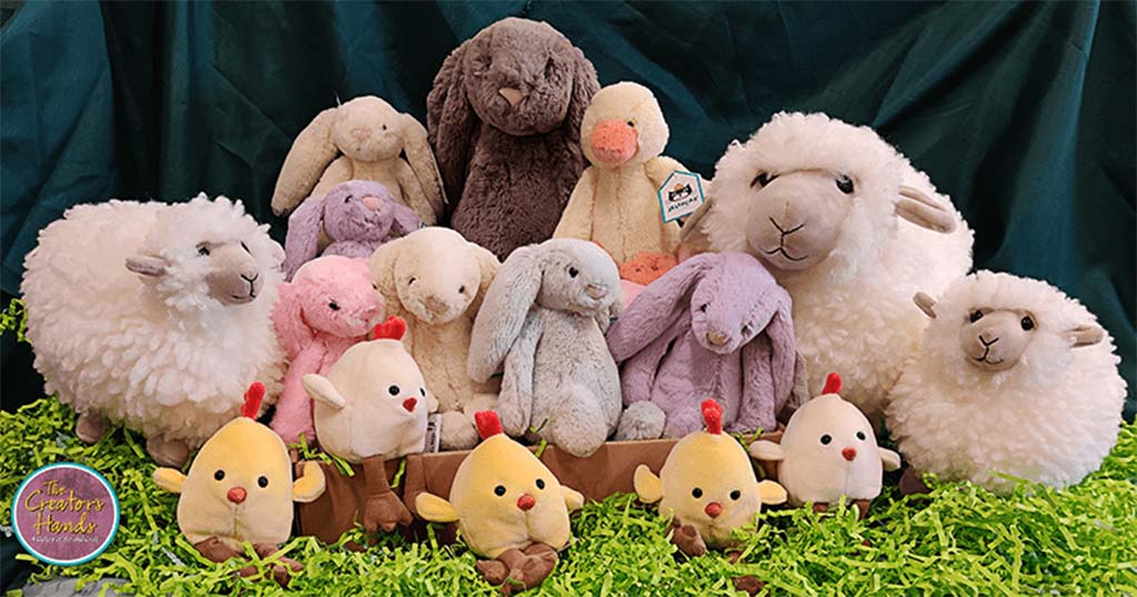 A collection of plush toys including bunnies, sheep, and chicks arranged on artificial grass with a dark green fabric background.