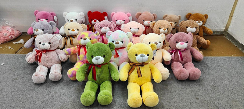 A large group of colorful teddy bears in various pastel and bright shades arranged in rows on the floor, each with a ribbon around its neck.