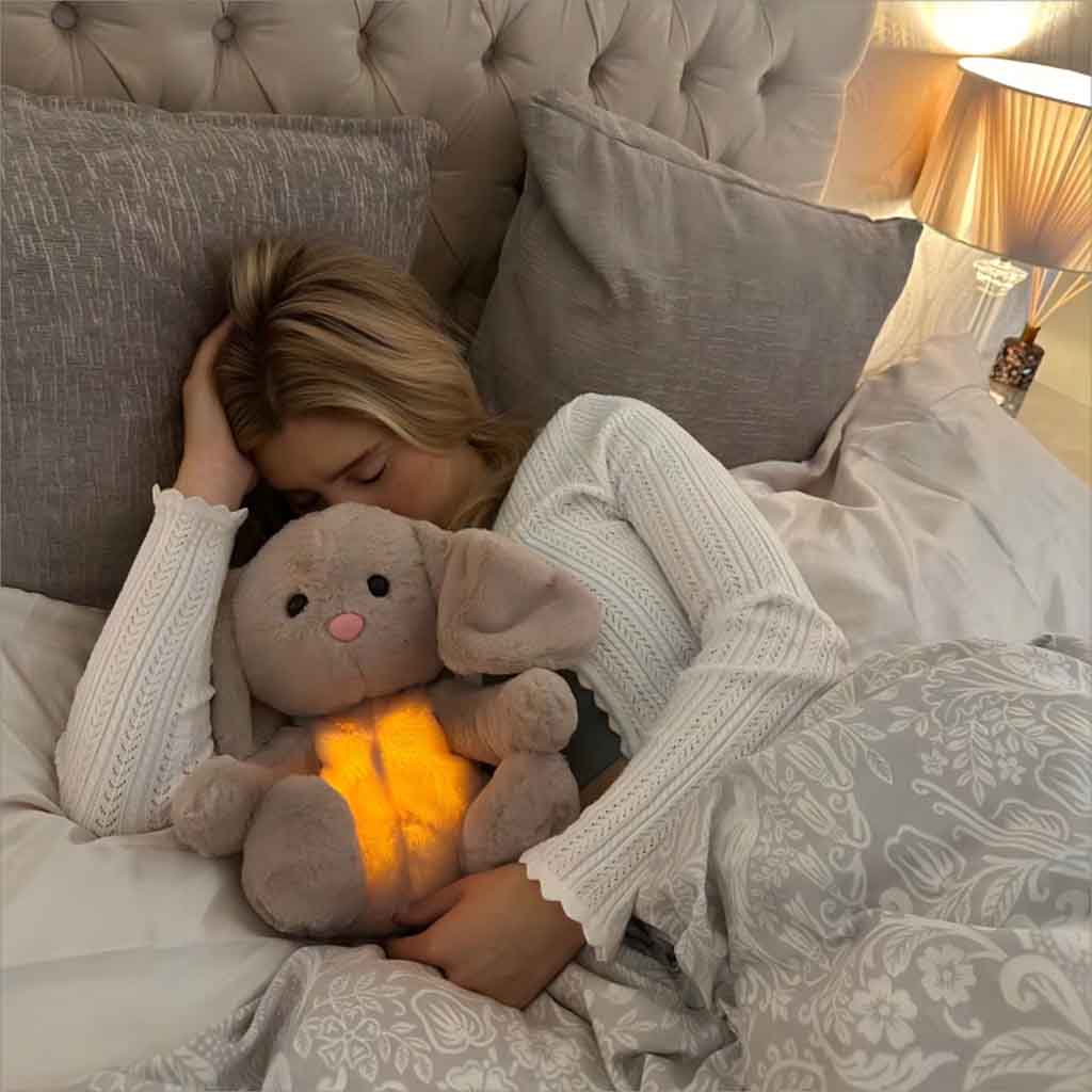 A girl sleeping in bed while holding a soft, glowing bunny plush toy, creating a warm and comforting atmosphere in a dimly lit bedroom.