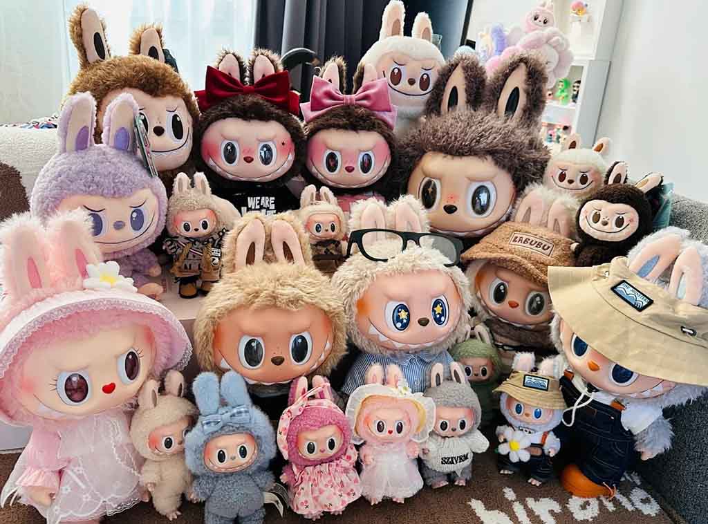 Large group of Labubu plush toys in various sizes, colors, and outfits displayed together on a couch, showing detailed bunny-ear designs and expressive faces.
