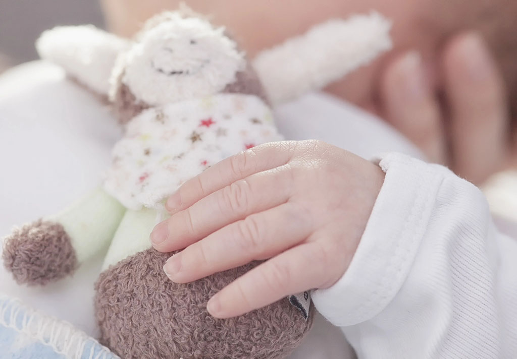 Close-up of a baby gently holding a small soft plush toy while resting, with focus on the infant’s hand and cuddly doll.