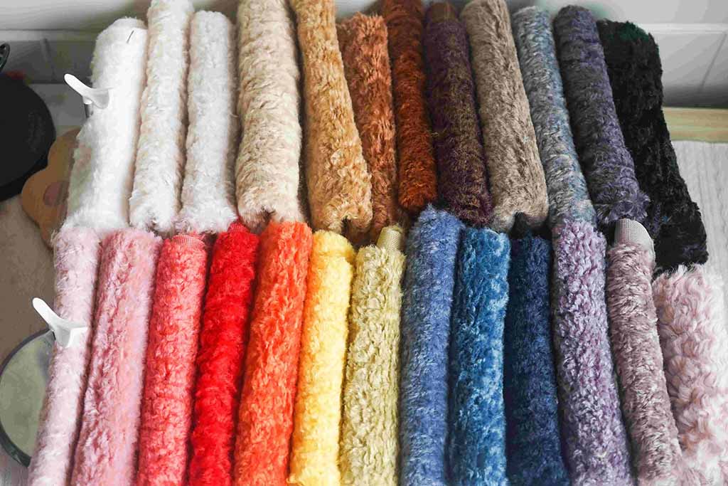 Multiple rolls of soft plush fabric in various colors including pink, brown, blue, yellow, and purple, neatly arranged for stuffed toy production.